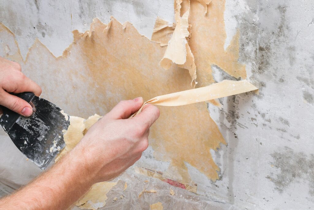 man-removes-old-wallpaper-with-spatula-spray-bottle-with-water-min - drywall repair silver spring md